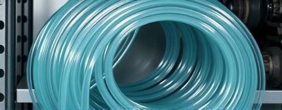 sleek clear PVC tubing, glossy surface, coiling intricately, photorealistic, arranged on a metal shelve, surrounded by mechanical parts, highly detailed, glistening loops, 8K resolution, faint aqua tint, soft yet bright lighting, shot with a 70mm lens.